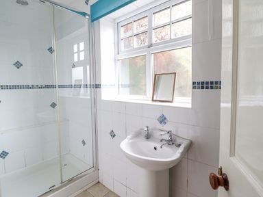 A bathroom with a pedestal sink a shower with glass doors and a window with a blue blind at Is Y Deri in Harlech