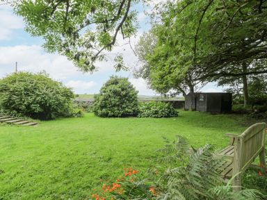 A garden with a wooden bench green grass shrubs and a small shed at Is Y Deri in Harlech