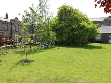 A grassy garden with trees benches a stone building and cars at Iona 10 Palace Street East in Berwick-upon-Tweed