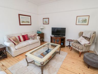 A living room with a sofa and armchair with cushions a glass coffee table a television on a stand and framed pictures on the walls at Iona 10 Palace Street East in Berwick-upon-Tweed