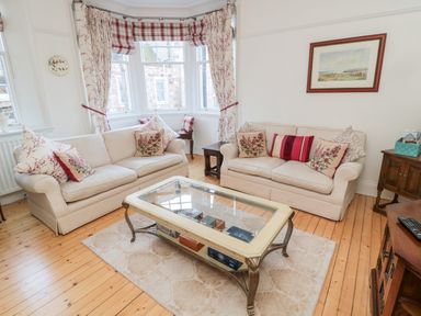 A living room with two beige sofas with cushions a glass coffee table and a window with curtains at Iona 10 Palace Street East in Berwick-upon-Tweed