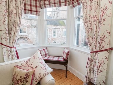 A window nook with a wooden bench and plaid cushions and floral curtains at Iona 10 Palace Street East in Berwick-upon-Tweed