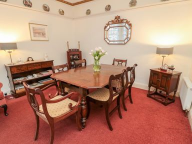 A dining room with a wooden table and six chairs with a vase of flowers on the table a sideboard a small cabinet two lamps and a decorative mirror at Iona 10 Palace Street East Berwick-upon-Tweed