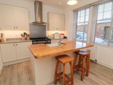 A kitchen with a wooden island counter with sink and two stools near window at Iona 10 Palace Street East in Berwick upon Tweed