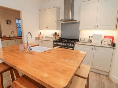 A kitchen with a wooden island countertop with a sink and stools and cabinets with a stove at Iona 10 Palace Street East in Berwick-upon-Tweed