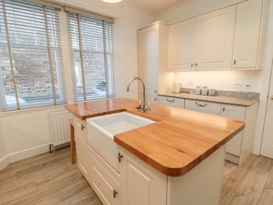 A kitchen with wooden countertops a white farmhouse sink white cabinets and windows with blinds at Iona 10 Palace Street East in Berwick-upon-Tweed