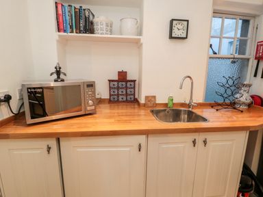 A kitchen counter with a microwave sink a clock books and kitchen containers at Iona 10 Palace Street East in Berwick-upon-Tweed