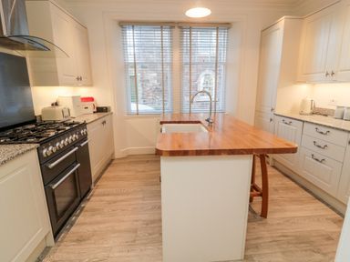 A kitchen with wooden countertops a black stove white cabinets and a window with blinds at Iona 10 Palace Street East in Berwick-upon-Tweed