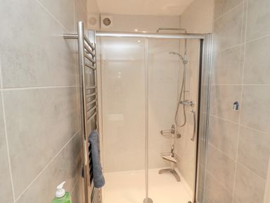 A bathroom shower area with sliding glass doors a chrome showerhead a towel rack with a blue towel and tiled walls at Iona 10 Palace Street East in Berwick-upon-Tweed