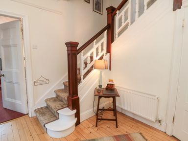 A staircase with carpeted steps and wooden banister next to a small table with a lamp and a radiator on the wall at Iona 10 Palace Street East in Berwick-upon-Tweed