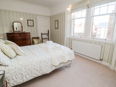A bedroom with a bed a wooden dresser two chairs and windows at Iona 10 Palace Street East in Berwick-upon-Tweed