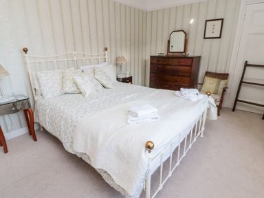 A bedroom with a bed with white and patterned bedding a wooden dresser a chair and bedside tables at Iona 10 Palace Street East in Berwick-upon-Tweed