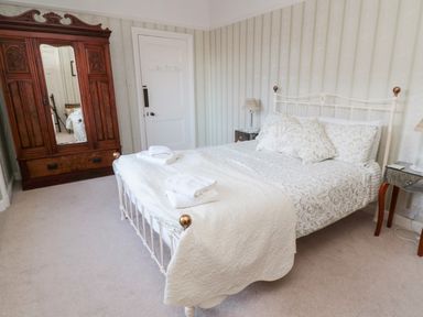 A bedroom with a bed with patterned pillows and blankets two bedside tables with lamps an antique wooden wardrobe and a closed door at Iona 10 Palace Street East in Berwick-upon-Tweed