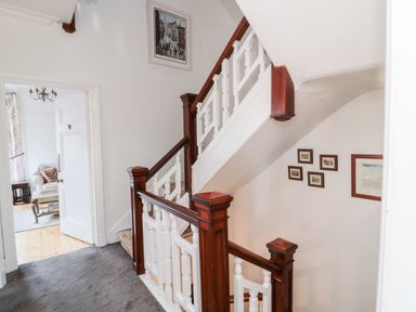 A staircase with wooden banisters and framed pictures on the wall near a doorway leading to a living room at Iona 10 Palace Street East in Berwick-upon-Tweed
