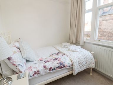 A bedroom with a single bed with floral bedding and folded towels on top at Iona 10 Palace Street East in Berwick-upon-Tweed