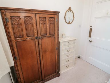A wooden wardrobe and a white chest of drawers with a decorative mirror on the wall at Iona 10 Palace Street East in Berwick-upon-Tweed