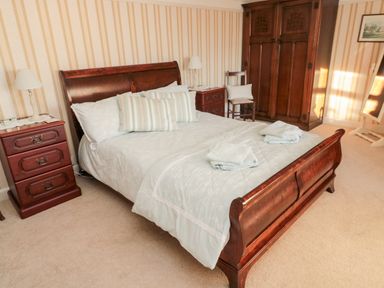 A bedroom with a wooden bed, bedside tables with lamps, an armoire, a chair and a standing mirror at Iona 10 Palace Street East Berwick-upon-Tweed