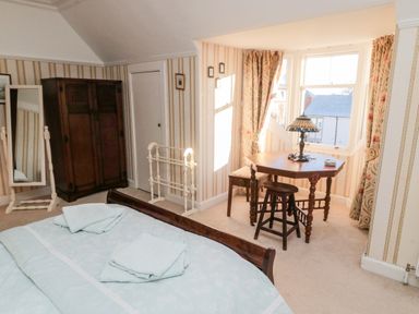 A bedroom with a bed folded towels wardrobe standing mirror wooden table chairs and a lamp by bay windows at Iona 10 Palace Street East in Berwick-upon-Tweed