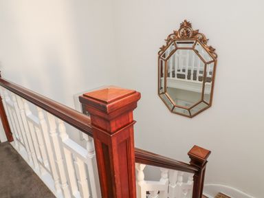 A wooden staircase with white balusters and a decorative wall mirror at Iona 10 Palace Street East in Berwick-upon-Tweed