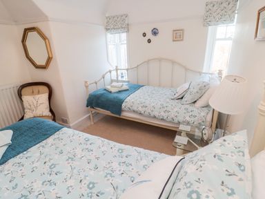 A bedroom with two single beds floral bedding a chair with a cushion a wall mirror and a bedside table with a lamp at Iona 10 Palace Street East in Berwick-upon-Tweed