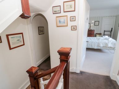A stairwell with wood handrails leading to a hallway with framed artwork and a bedroom with a bed and dresser visible at Iona 10 Palace Street East in Berwick-upon-Tweed