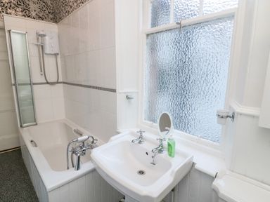 A bathroom with a bathtub a sink a window and patterned wallpaper at Iona 10 Palace Street East in Berwick-upon-Tweed