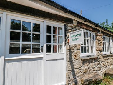 Exterior of a stone building with white framed windows and doors with a sign reading Treverbyn Smithy in St Neot