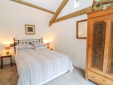 A bedroom with a double bed bedside tables with lamps a wooden wardrobe and exposed wooden beams at Treverbyn Smithy St Neot