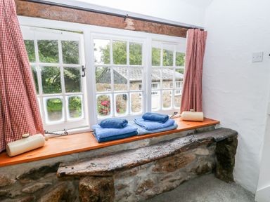 A window with red check curtains folded blue towels and ceramic bottles on the sill at Treverbyn Smithy in St Neot