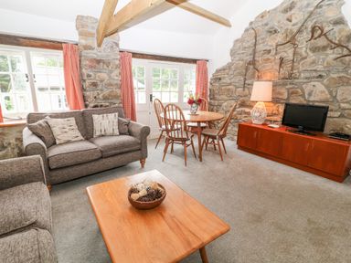 A living room with gray sofas a wooden coffee table a dining table with chairs and a TV on a wooden cabinet at Treverbyn Smithy in St Neot