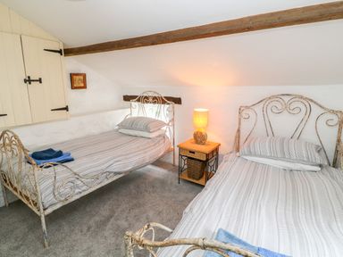 A bedroom with two single metal frame beds and a small bedside table with a lamp at Treverbyn Smithy in St Neot