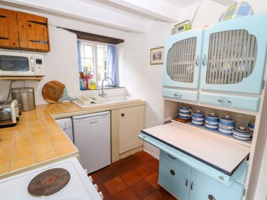 A kitchen with a blue cupboard holding striped jars and a microwave on a wooden shelf at Treverbyn Smithy in St Neot