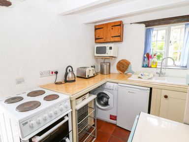 A small kitchen with a stove washing machine fridge microwave kettle toaster and sink at Treverbyn Smithy in St Neot