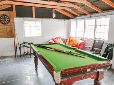 A game room with a pool table two pool cues a dartboard a small table a sofa and chairs at Treverbyn Smithy in St Neot