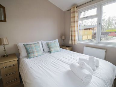 A bedroom with a bed with white bedding and plaid pillows two bedside tables with lamps and a window with plaid curtains at 22 Thirlmere in Troutbeck Bridge
