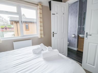 A bedroom with a made bed and rolled towels near an open door leading to a bathroom at 22 Thirlmere in Troutbeck Bridge