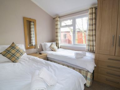 A bedroom with two beds a wooden wardrobe a bedside table with a lamp and mirror at 22 Thirlmere in Troutbeck Bridge