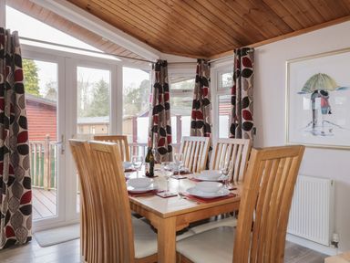 A dining room with a wooden table set for six with wine glasses and plates near glass doors with patterned curtains at 22 Thirlmere in Troutbeck Bridge