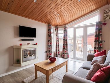 A living room with a wooden coffee table a grey sofa with cushions patterned curtains and a wall-mounted television at 22 Thirlmere in Troutbeck Bridge