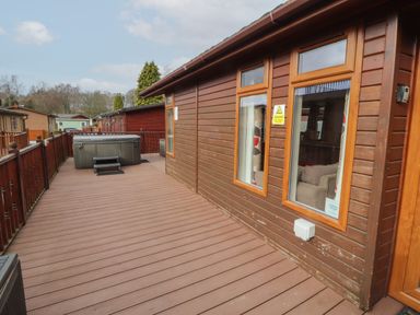 A deck with a fenced railing and a hot tub outside wooden cabins at 22 Thirlmere in Troutbeck Bridge