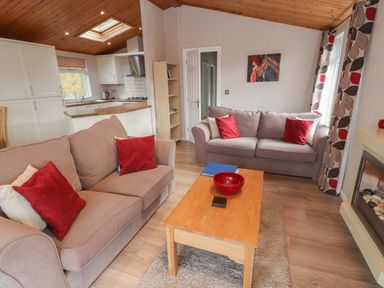 A living room with two sofas red cushions wooden coffee table and open kitchen at 22 Thirlmere in Troutbeck Bridge