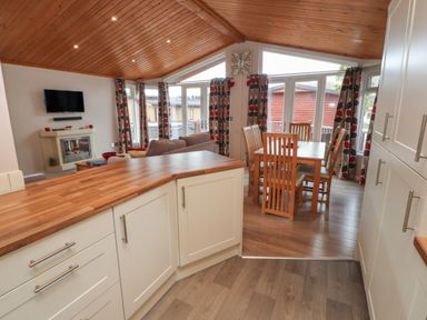A kitchen with wood countertops overlooking a dining area with a wooden table and chairs and a living area with a sofa a television and a fireplace at 22 Thirlmere in Troutbeck Bridge