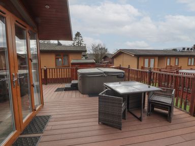 A wooden deck with a hot tub table and chairs outside wooden lodges at 22 Thirlmere in Troutbeck Bridge
