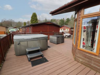 A wooden deck with a covered hot tub and seating area outside wooden cabins at 22 Thirlmere in Troutbeck Bridge