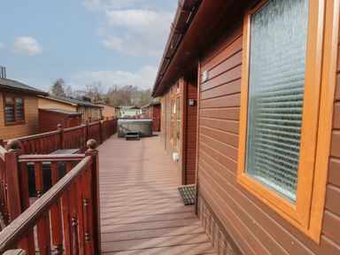 An outdoor wooden deck with railing and hot tub outside several wooden cabins at 22 Thirlmere in Troutbeck Bridge