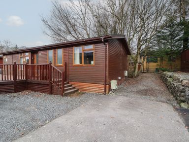 A single-story wooden cabin with steps and railing surrounded by trees and gravel driveway at 22 Thirlmere in Troutbeck Bridge