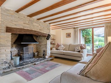A living room with two sofas a stone fireplace and large window at West End Barn in Cleeve Prior near Evesham