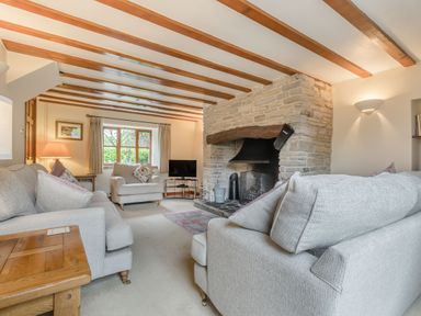 A living room with sofas a stone fireplace and wooden beams on the ceiling at West End Barn Cleeve Prior near Evesham