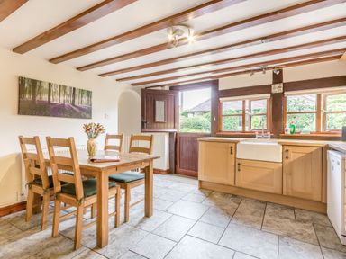 A kitchen with wooden cabinets a farmhouse sink dining table with chairs and an open door at West End Barn in Cleeve Prior near Evesham