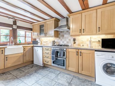 A kitchen with wooden cabinets a dishwasher an oven a washing machine and a window at West End Barn in Cleeve Prior near Evesham